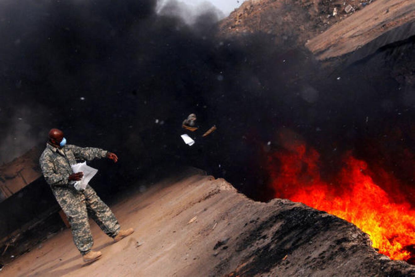 An Air Force master sergeant tosses unserviceable uniform items into a burn pit at Balad Air Base, Iraq, on March 10, 2008.